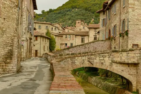Antica via acciottolata con un ponte in pietra su un ruscello, circondata da case in pietra. Un'immagine perfetta dei borghi da visitare in Umbria.