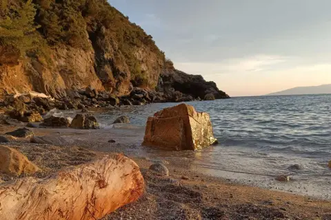 Spiaggia di Cala del Gesso al tramonto, con scogli dorati e un tronco sulla riva.