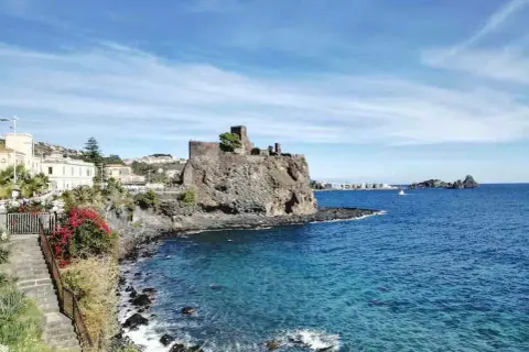 Castello normanno su scogliera lavica, un gioiello tra le cose da vedere a Catania e dintorni. Mare azzurro e case bianche.