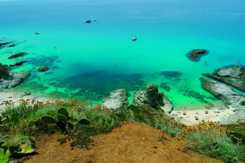 Vista dall'alto di una baia con acqua cristallina e spiagge dorate, tra le spiagge più belle della Calabria. Rocce e vegetazione mediterranea incorniciano il paesaggio.