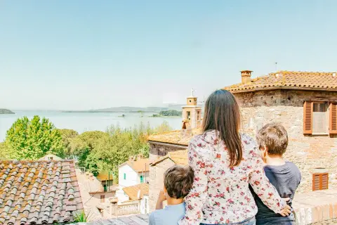 Una madre e due bambini ammirano un lago e un borgo italiano, scoprendo luoghi magici per bambini in Italia.