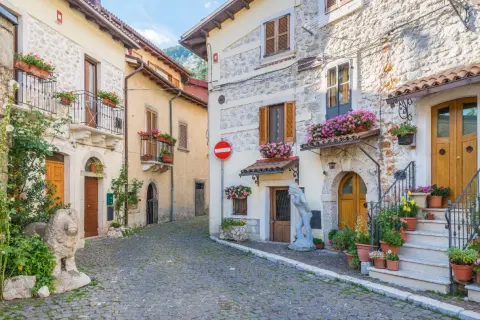 Cobblestone street in a medieval Italian village with stone buildings, balconies, and potted flowers.