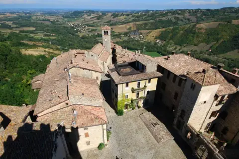 Vista aerea del borgo di Vigoleno, con tetti in cotto e un campanile che domina il paesaggio collinare.