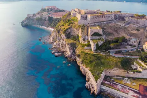 Fortificazioni storiche su una scogliera a picco sul mare turchese, un gioiello delle città della Toscana.