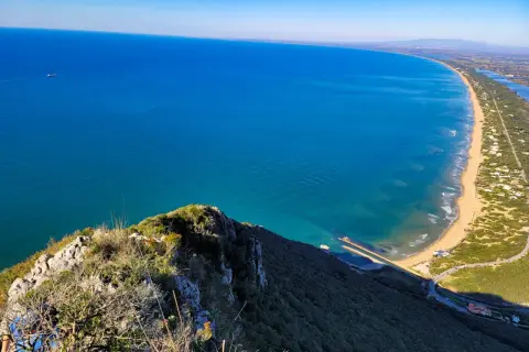 Vista dall'alto del promontorio del Circeo, con il mare azzurro, la spiaggia dorata e la vegetazione lussureggiante.