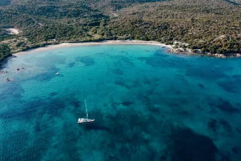 Vista aerea di una baia con acque cristalline, una barca a vela e una spiaggia dorata. Un assaggio delle migliori spiagge Costa Smeralda.