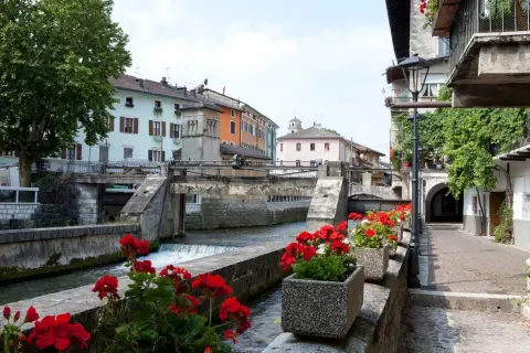 Un pittoresco canale attraversa il borgo Val Sugana, fiancheggiato da case colorate e gerani rossi in fiore.
