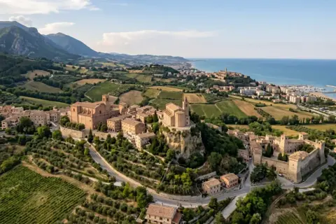 Borghi da visitare vicino Ascoli Piceno: un castello medievale e chiese storiche su colline verdi, con il mare all'orizzonte.