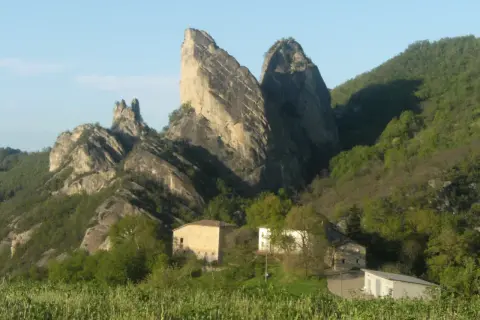 I Sassi di Roccamalatina, imponenti formazioni rocciose, dominano un paesaggio verdeggiante con casolari sparsi.