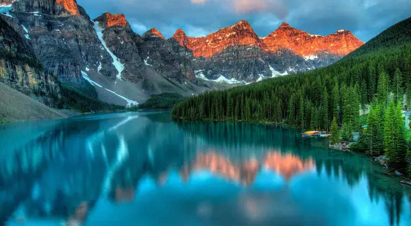 Lago turchese riflette le montagne italiane più famose, con foreste di conifere e cielo nuvoloso.