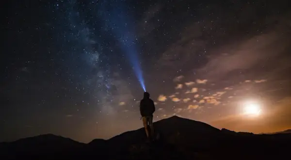 Persona su una montagna di notte, illuminata da una torcia, sotto un cielo stellato mozzafiato.