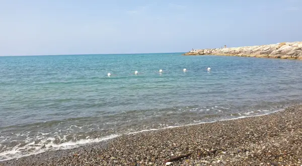 Spiaggia di ciottoli a Cecina, con mare calmo e un molo in lontananza. Perfetto per scoprire cosa vedere e rilassarsi.