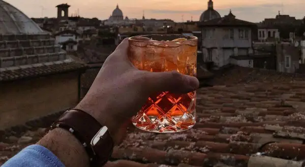 Un bicchiere di aperitivo con vista sui tetti di Roma centro al tramonto. Un momento perfetto per un apericena indimenticabile.
