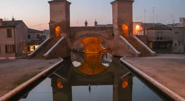Ponte di barche a Comacchio, uno dei borghi medievali vicino a Ferrara, con le sue torri illuminate e il riflesso sull'acqua.