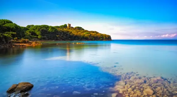 Torre medievale su una collina verdeggiante che si affaccia su acque cristalline, una delle punta ala spiagge più belle.