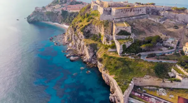 Fortificazioni storiche su una costa rocciosa con mare blu intenso. Un'idea per cosa visitare in Toscana in 2 giorni, tra storia e natura.