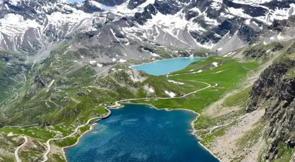 Laghi alpini e strada tortuosa sul colle del Nivolet, con montagne innevate sullo sfondo.