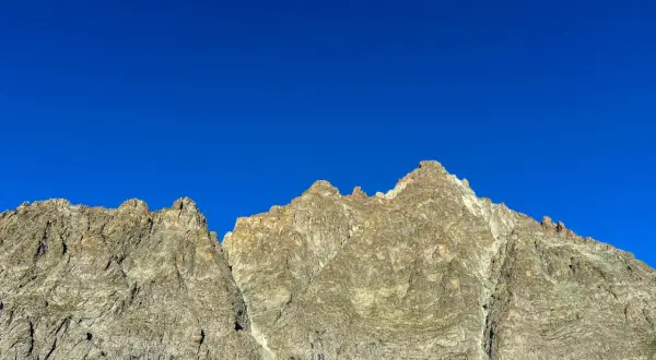 Cime rocciose del Monviso, con la via normale che sale verso la vetta sotto un cielo azzurro intenso.