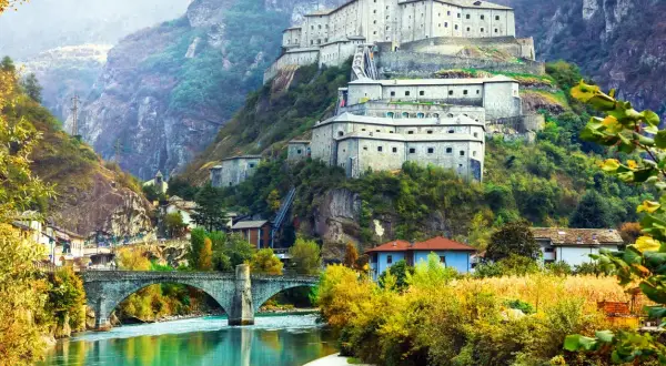 Fortezza imponente su un colle, con un fiume turchese e un ponte ad arco. Un paesaggio da fiaba tra Piemonte e Valle d'Aosta.