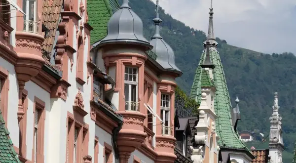 Edifici storici con torrette e tetti verdi, un assaggio di cosa vedere a Bolzano in un giorno, con montagne sullo sfondo.