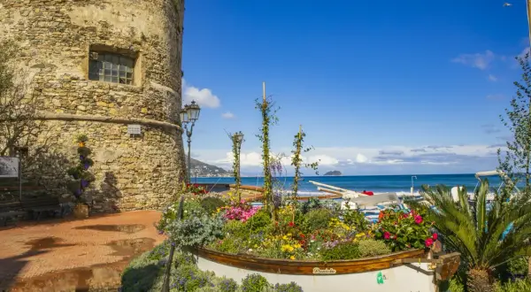 Laigueglia centro storico: torre medievale, barca fiorita e mare blu.