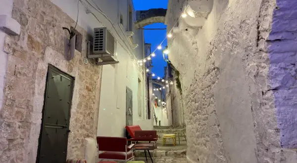 Un vicolo suggestivo con luci soffuse, sedute colorate e un arco in pietra. Perfetto per scoprire cosa vedere vicino Alberobello.