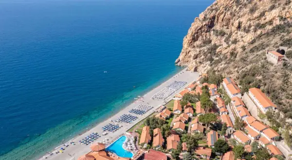 Villaggio turistico con spiaggia attrezzata e piscina, incastonato tra il mare blu e una scogliera rocciosa. Un luogo ideale per esplorare i paesi vicino Catania sul mare.