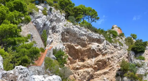 Scogliera rocciosa con una scalinata in mattoni che sale verso la cima, dove si intravede un rudere. Si immagina il **salto di Tiberio**.