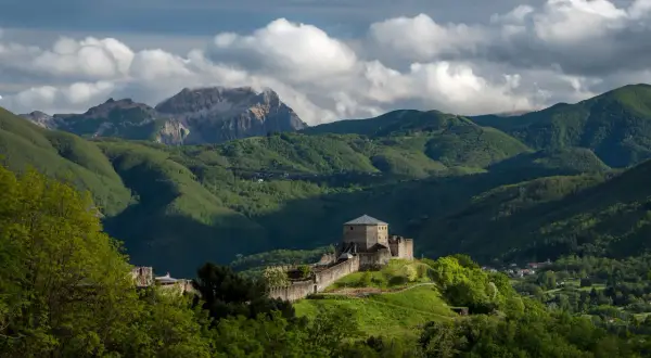 Roccia fortificata nella Garfagnana, dove si trova un castello medievale su una collina verdeggiante, con montagne sullo sfondo.