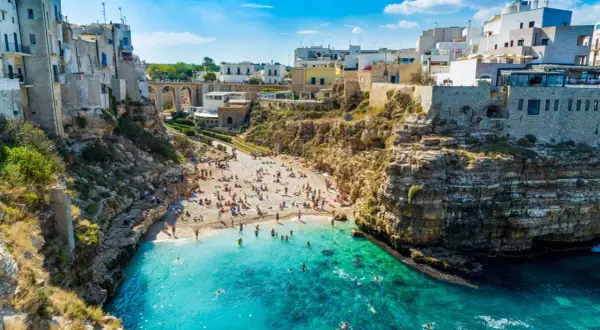Una baia con spiaggia affollata e case bianche a picco sul mare turchese, una delle splendide spiagge vicino Bari.