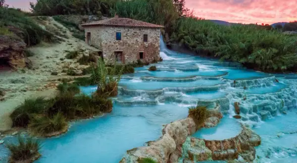 Cascate termali turchesi con un antico mulino in pietra, uno dei tanti posti belli in Toscana, al tramonto.