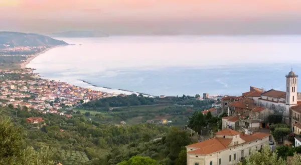 Panoramica di borghi del Cilento da visitare, con case arroccate su colline verdi che scendono verso il mare azzurro.