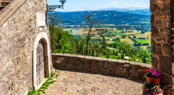 Un vicolo acciottolato a Bassano in Teverina conduce a un panorama mozzafiato di colline verdi e campi coltivati sotto un cielo azzurro.