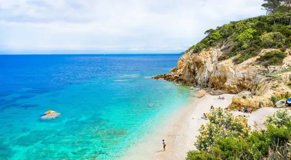 Spiaggia incantevole con acque cristalline, rocce dorate e vegetazione lussureggiante. Un angolo di paradiso, quasi un mare vicino Firenze, dove rilassarsi.