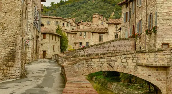 Antica via acciottolata con un ponte in pietra su un ruscello, circondata da case in pietra. Un'immagine perfetta dei borghi da visitare in Umbria.