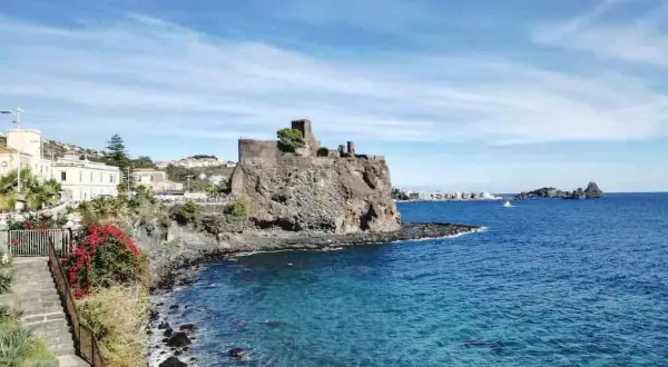 Castello normanno su scogliera lavica, un gioiello tra le cose da vedere a Catania e dintorni. Mare azzurro e case bianche.
