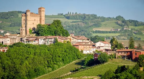 Borgo medievale con castello domina colline verdi e vigneti, un paesaggio tipico delle Langhe e Monferrato.
