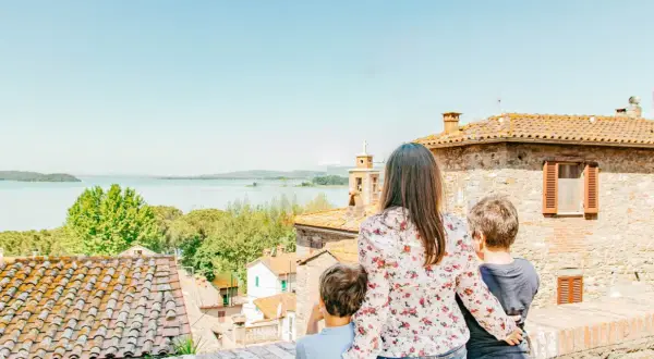 Una madre e due bambini ammirano un lago e un borgo italiano, scoprendo luoghi magici per bambini in Italia.
