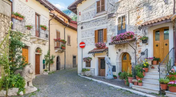 Cobblestone street in a medieval Italian village with stone buildings, balconies, and potted flowers.