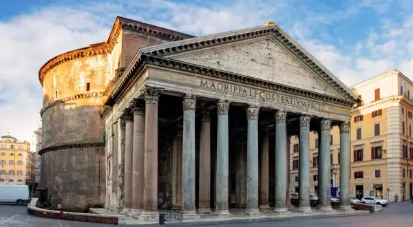 Il Pantheon, una delle chiese particolari di Roma, con il suo portico colonnato e la cupola imponente, si staglia sotto un cielo azzurro.