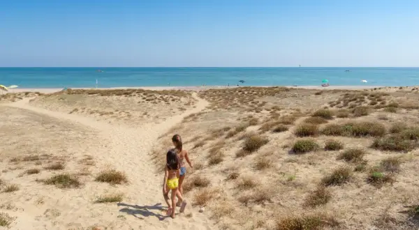 Due bambine corrono verso il mare in Abruzzo, tra dune sabbiose e macchia mediterranea.