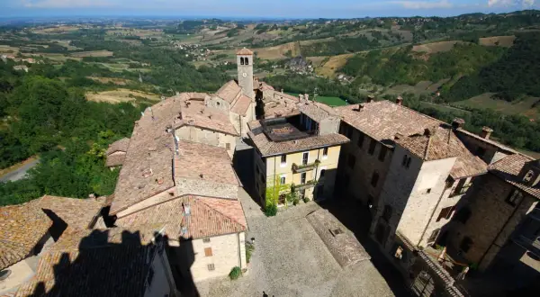 Vista aerea del borgo di Vigoleno, con tetti in cotto e un campanile che domina il paesaggio collinare.