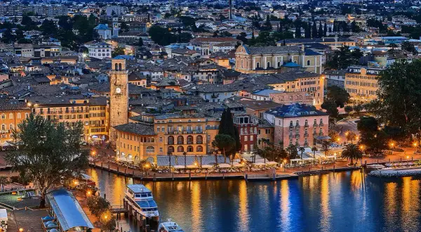 Incantevole vista serale di un borgo sul lago, con edifici colorati, un campanile e barche illuminate. Un gioiello tra i paesi del Trentino Alto Adige.