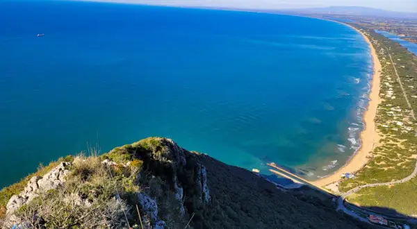 Vista dall'alto del promontorio del Circeo, con il mare azzurro, la spiaggia dorata e la vegetazione lussureggiante.
