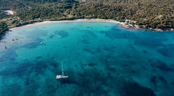 Vista aerea di una baia con acque cristalline, una barca a vela e una spiaggia dorata. Un assaggio delle migliori spiagge Costa Smeralda.