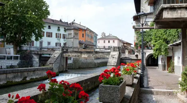 Un pittoresco canale attraversa il borgo Val Sugana, fiancheggiato da case colorate e gerani rossi in fiore.