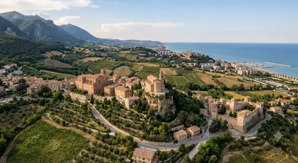 Borghi da visitare vicino Ascoli Piceno: un castello medievale e chiese storiche su colline verdi, con il mare all'orizzonte.