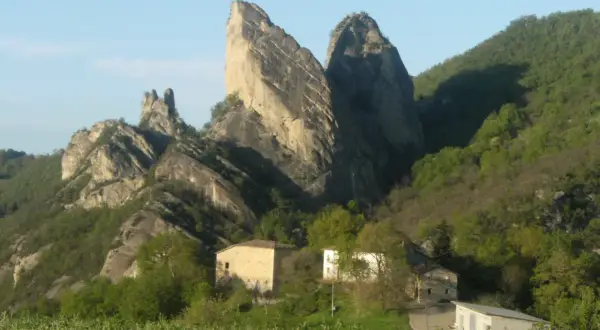 I Sassi di Roccamalatina, imponenti formazioni rocciose, dominano un paesaggio verdeggiante con casolari sparsi.