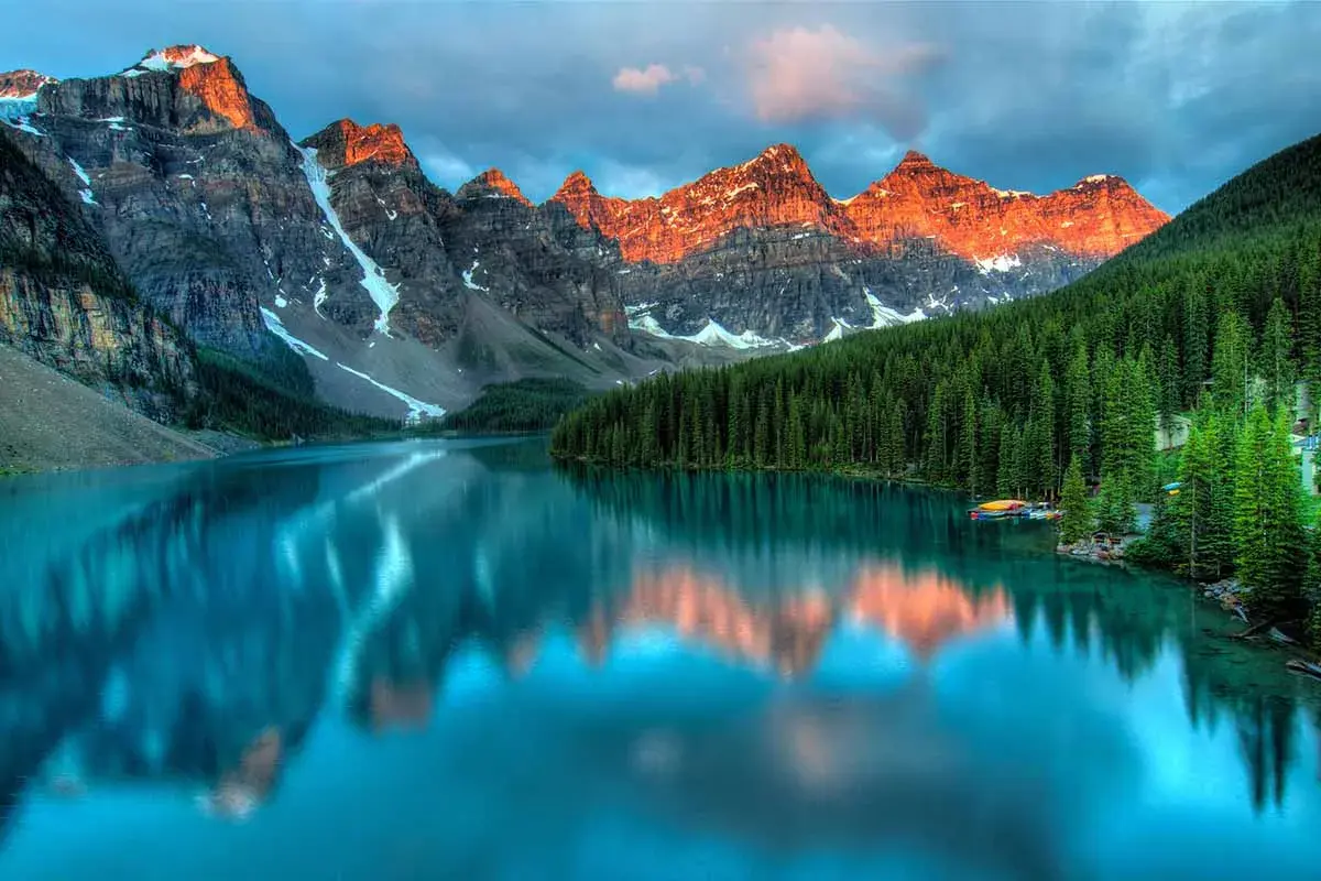 Lago turchese riflette le montagne italiane più famose, con foreste di conifere e cielo nuvoloso.