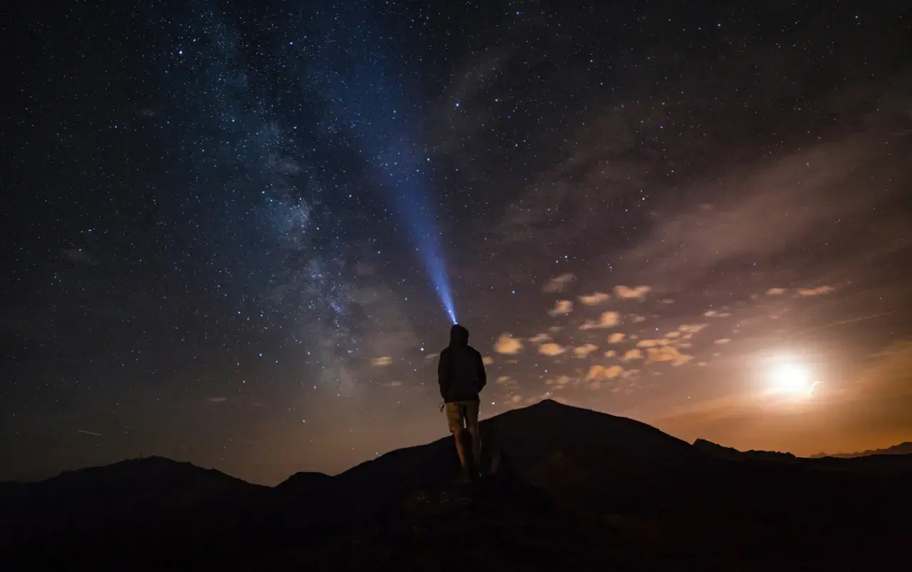 Persona su una montagna di notte, illuminata da una torcia, sotto un cielo stellato mozzafiato.